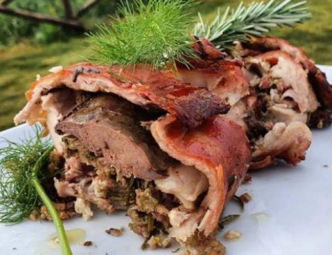 Arrosto ripieno con erbe aromatiche su piatto bianco.