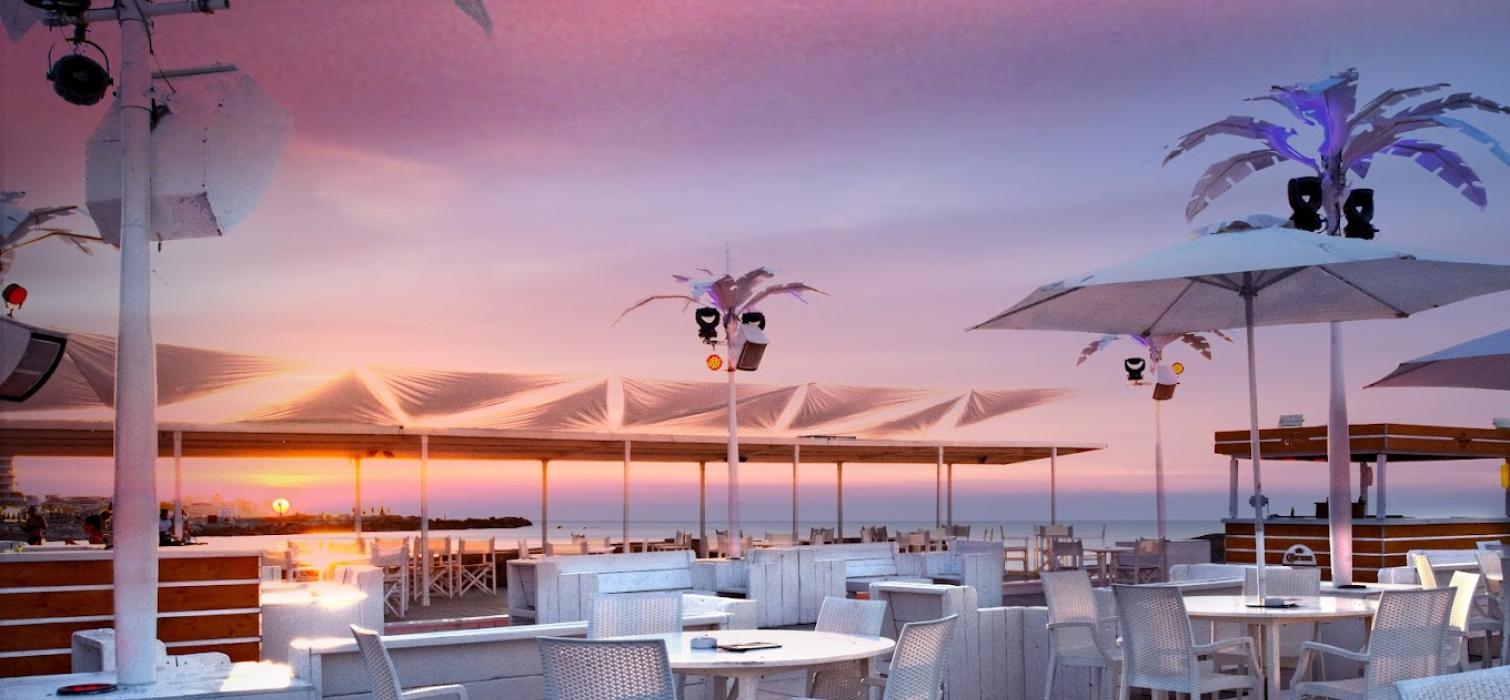 Terrazza sul mare con tavoli e sedie bianche al tramonto.