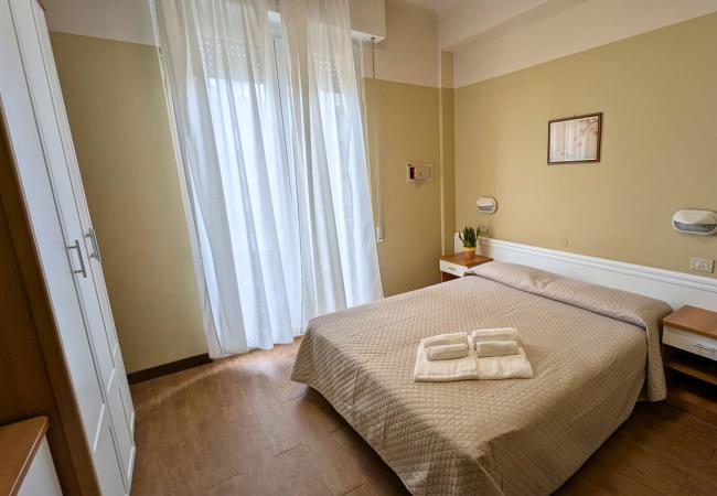 Camera semplice e luminosa, letto matrimoniale, tende bianche, atmosfera accogliente.